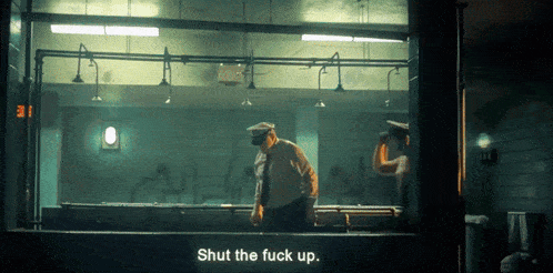 a man is standing in a dark room with a sign that says shut the fuck up