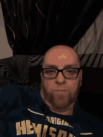a man wearing glasses and a shirt that says hemingway is laying on a bed