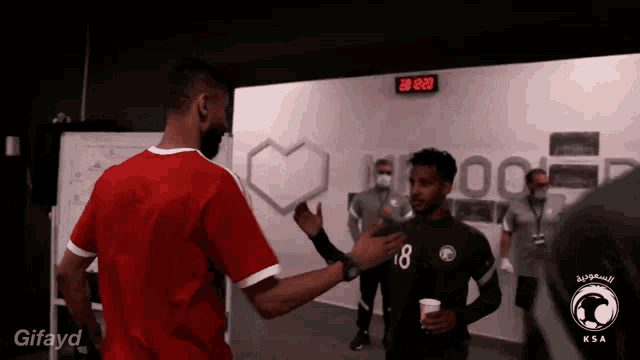 a man wearing a red shirt with the number 18 on it shakes hands with another man