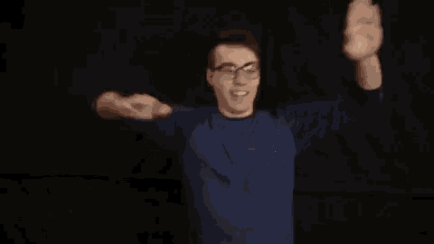 a young man wearing glasses and a blue shirt is making a funny face with his arms outstretched .