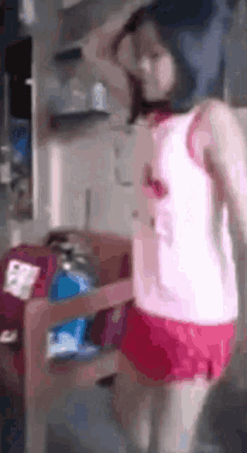 a woman in a pink shirt and red shorts is dancing in a kitchen .