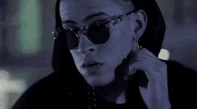 a young man wearing sunglasses and a black hoodie is talking on a cell phone