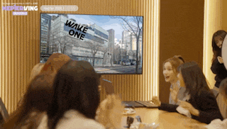 a group of people sitting around a table watching a tv that says wake one on it