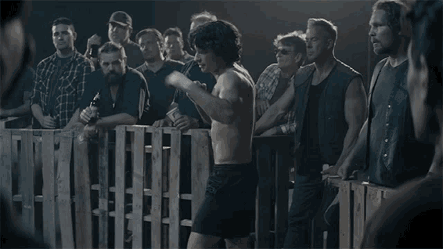 a man without a shirt is standing in front of a crowd of men