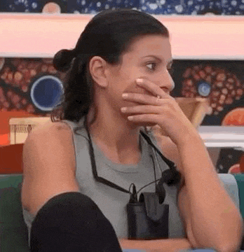 a woman is sitting on a couch with her hand over her mouth .