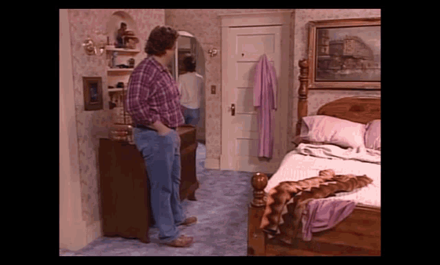 a man in a plaid shirt stands in a bedroom with a bed