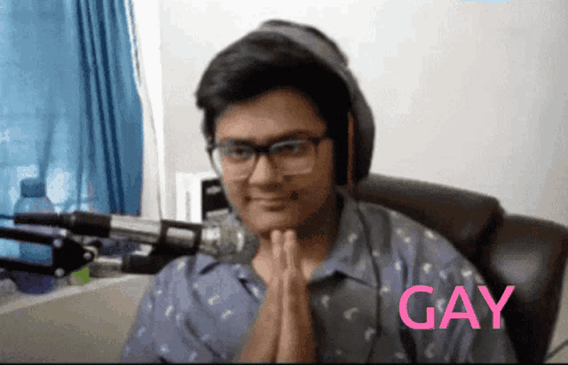 a man wearing headphones and glasses is praying with the word gay behind him