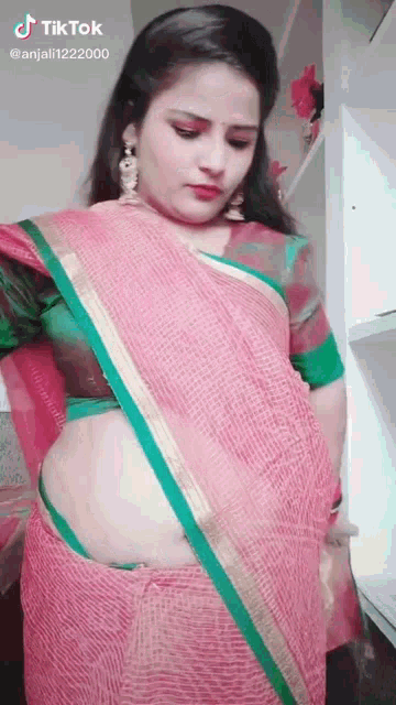 a woman in a pink saree with a green border is standing in a kitchen .
