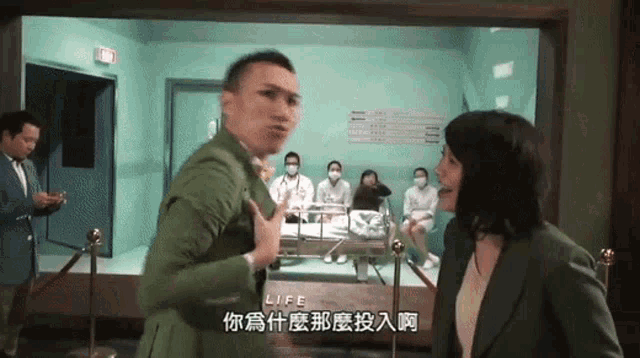 a man in a green suit is talking to a woman in front of a screen that says " life "