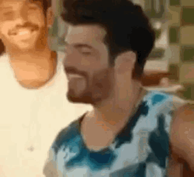a man with a beard is smiling while standing next to another man in a white shirt .