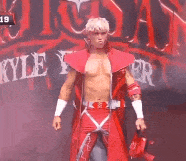 a man in a red wrestling outfit is standing in front of a sign that says kyle yzer .