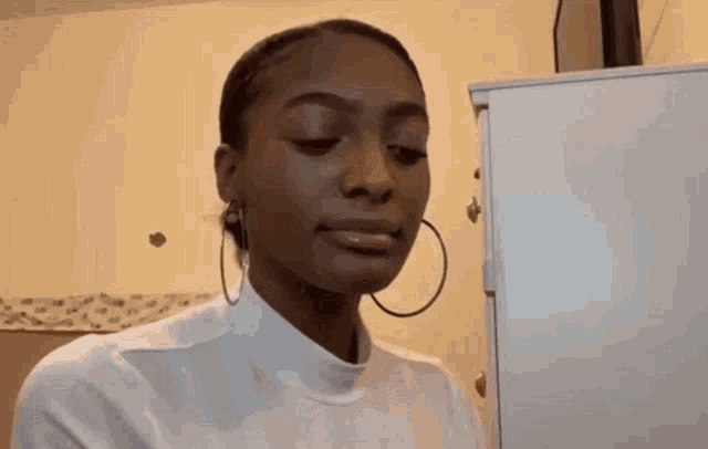 a woman is applying lip gloss to her lips while standing in front of a refrigerator .