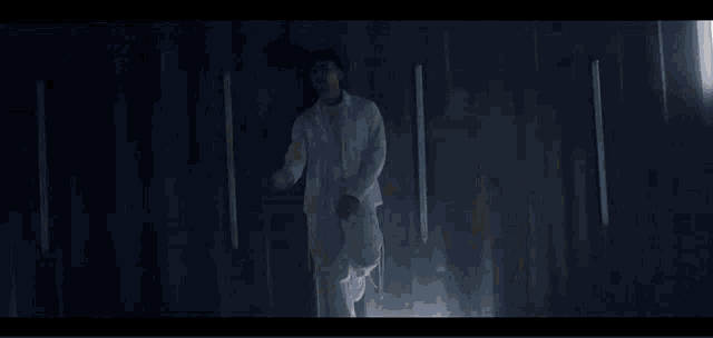 a man in a white suit is dancing in a dark room with lights on the walls .