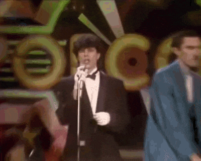 a man in a tuxedo is singing into a microphone on a stage in front of a crowd .