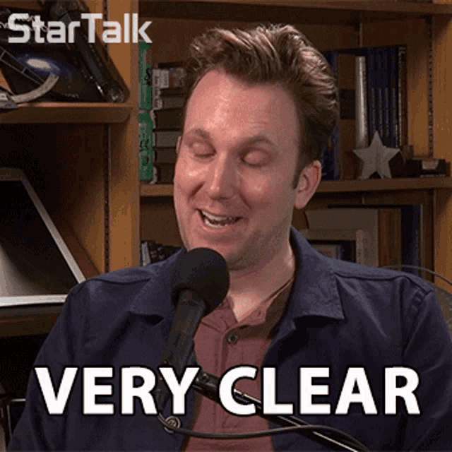 a man speaking into a microphone with the words " very clear " behind him