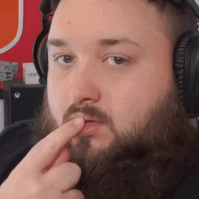 a man with a beard is wearing headphones and pointing at his mouth