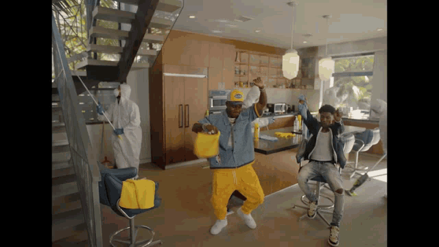 a man in a yellow hat is dancing in a kitchen with other men