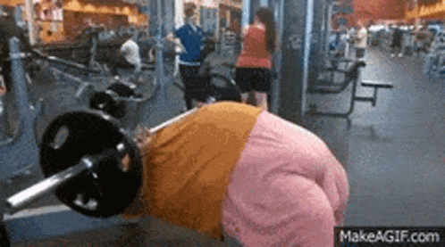 a woman in a pink shirt is lifting a barbell in a gym