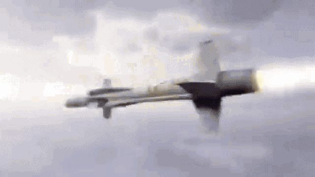 a fighter jet is flying through the air with a rocket coming out of its engine .