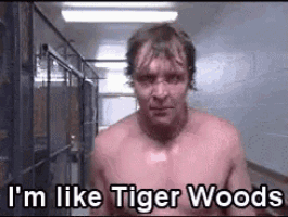 a shirtless man is standing in a hallway with the words `` i 'm like tiger woods '' written above him .