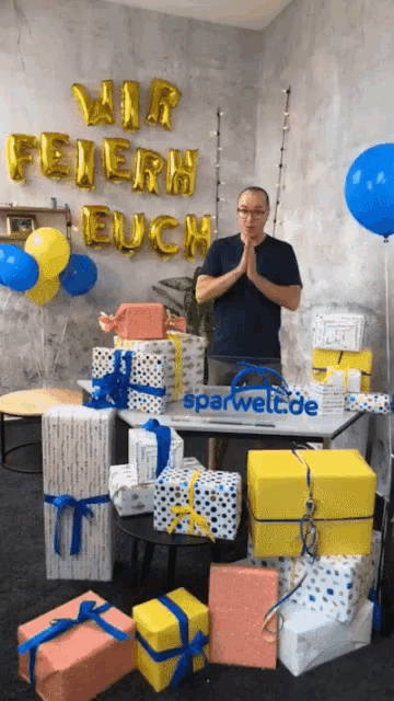 a man stands in front of a wall with wir feiern euch balloons behind him