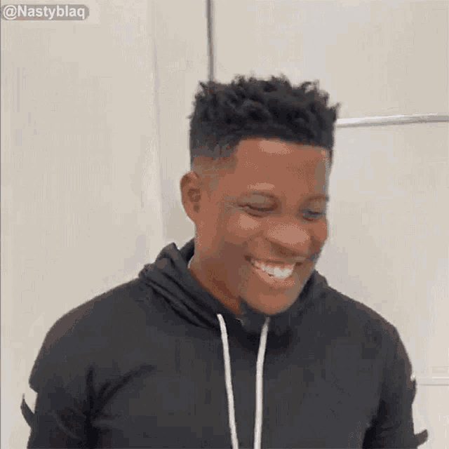 a man in a black hoodie is laughing with his eyes closed and his mouth open .