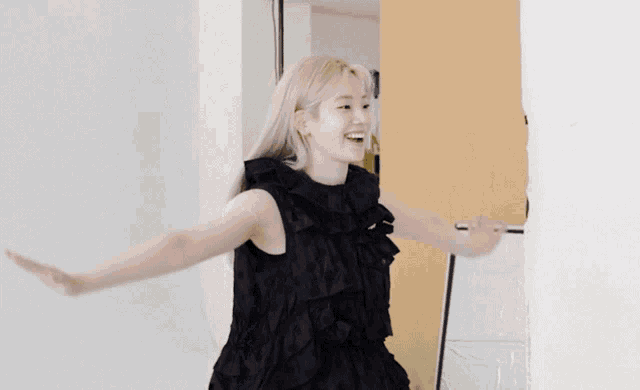 a woman in a black dress with ruffles on the sleeves is smiling with her arms outstretched
