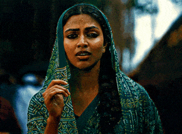 a woman wearing a green scarf around her head looks very sad