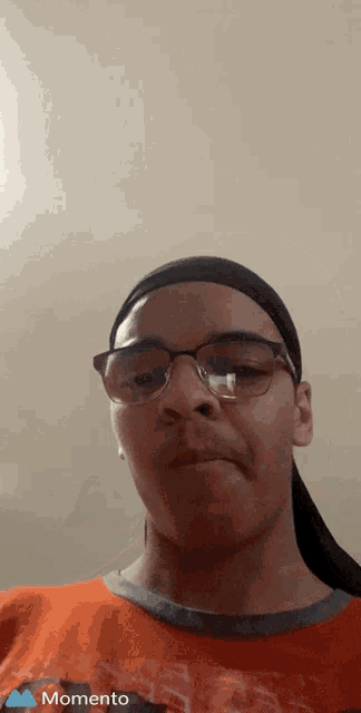 a young man wearing glasses and an orange shirt with the word momento on the bottom left