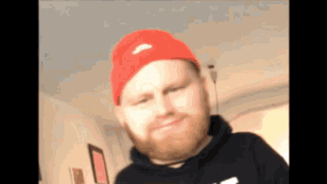 a man with a beard wearing a red hat and a black hoodie