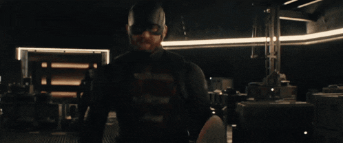 a man in a captain america uniform is standing in a dark room