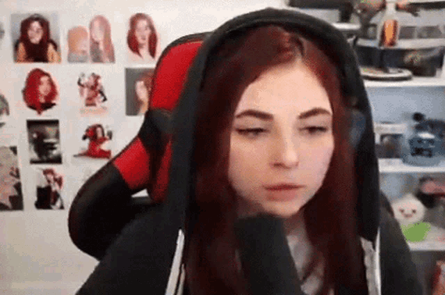 a woman with red hair is wearing a black hoodie and sitting in a red and black chair .
