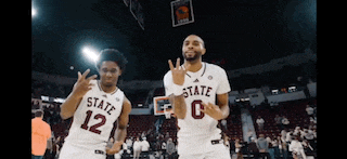 two basketball players wearing jerseys that say state 12 and 0 are celebrating on the court .