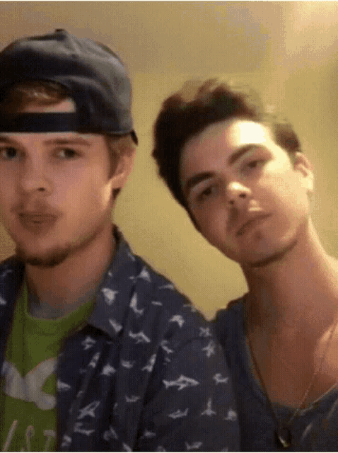 two young men are posing for a picture and one is wearing a hat and the other is wearing a shirt with birds on it