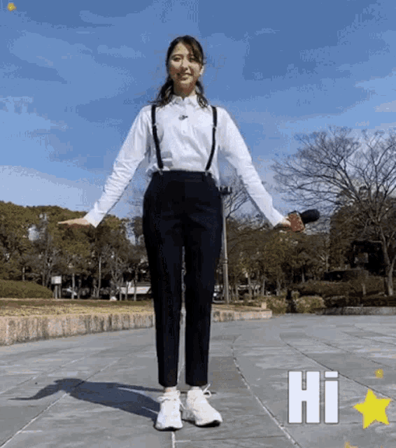 a woman wearing suspenders and a white shirt is standing on a sidewalk and says hi
