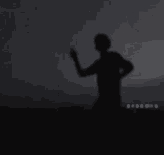 a silhouette of a man standing in the dark with his hand up .