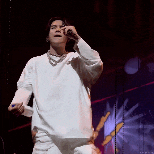 a man in a white shirt is singing into a microphone on stage
