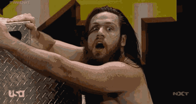 a shirtless wrestler is holding a metal item in front of a wwe nxt logo
