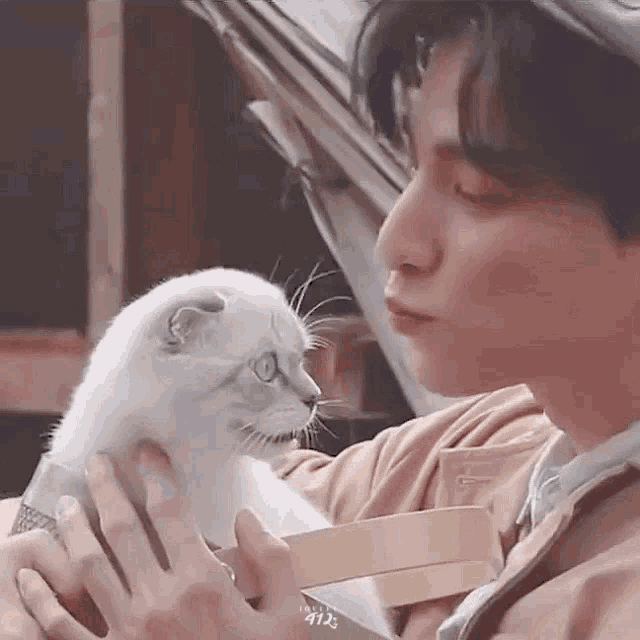 a man is holding a white cat in his arms and the cat is looking at the man .
