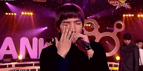 a man is singing into a microphone on a stage while covering his face .