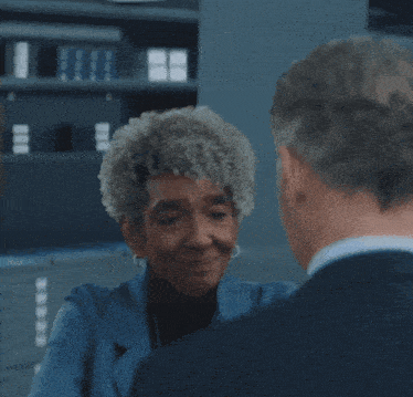 a woman in a blue jacket is smiling at a man in a suit