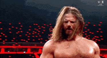 a man with long hair and a beard is standing in a wrestling ring without a shirt on .