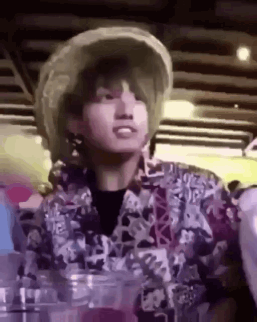 a young man wearing a straw hat and a floral shirt is sitting at a table .