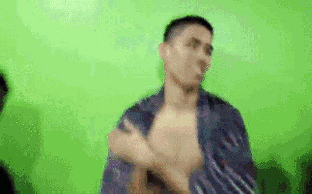 a man without a shirt is dancing in front of a green background .