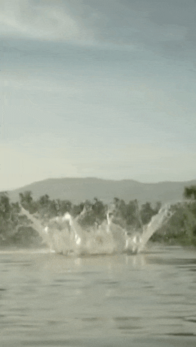 a person is swimming in a river with mountains in the background and a boat in the water .