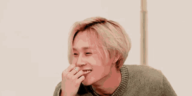 a young man with blonde hair and a ring on his finger is smiling and laughing .