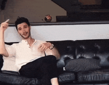 a man in a white shirt is sitting on a black couch and giving the middle finger