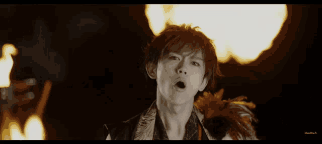 a man with a feather around his neck is standing in front of fire
