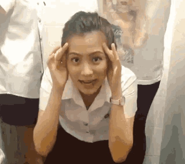 a woman in a white shirt and black skirt is holding her hands to her head .