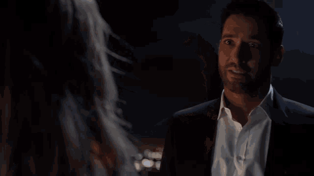 a man in a suit and white shirt is looking at a woman in a dark room